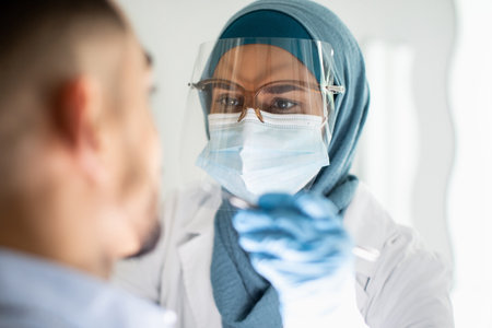 Islamic Dentist Lady In Hijab And Face Shield Examining Male Patients Teethの写真素材