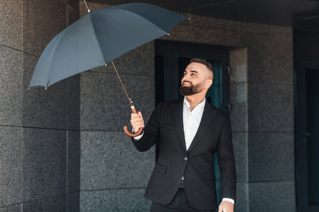 Mature office worker wearing classical suit holding umbrella while walking outdoors, going home after workの写真素材
