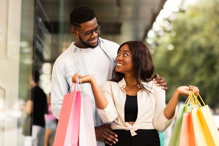 Beautiful black couple holding shopping bags looking at each otherの写真素材