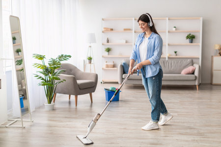 Cheerful woman listening to music cleaning floor with mopの写真素材
