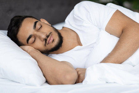 Calm Young Middle Eastern Man Sleeping Peacefully in Cozy Bed at Homeの写真素材