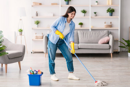 Smiling woman cleaning floor with string mop