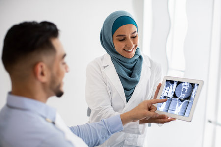Islamic Dentist Woman Showing Teeth Xray On Digital Tablet To Male Patientの写真素材