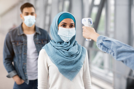 Flying During Coronavirus. Airport Staff Checking Muslim Female Passenger Temperature At Terminal