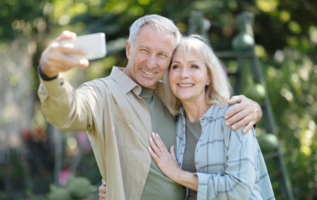 Happy elderly couple spending time in their garden together, taking selfies and smiling at cellphone...