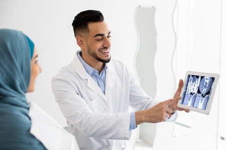 Arab Dentist Showing Teeth Xray On Digital Tablet To Muslim Female Patientの写真素材
