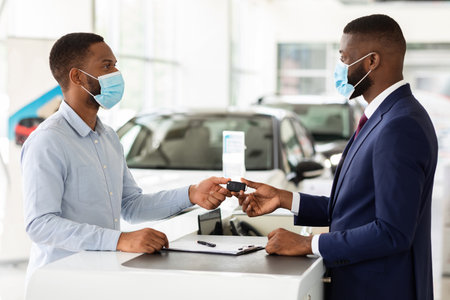 Car Showroom Manager Wearing Medical Mask Giving Key To Black Male Customer