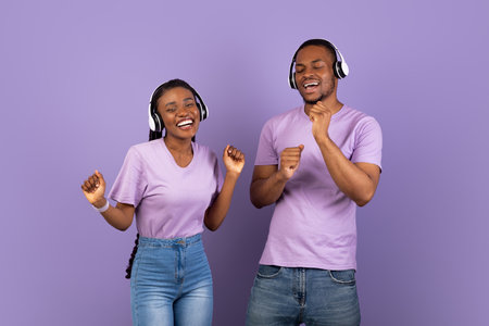 Portrait of emotional black couple in headphones dancing at studio