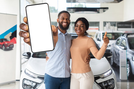 Happy Black Couple Standing Near New Car And Showing Blank Smartphoneの写真素材