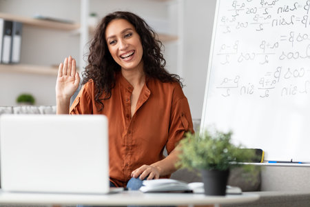 Smiling young woman teaching maths to students online, waving hello
