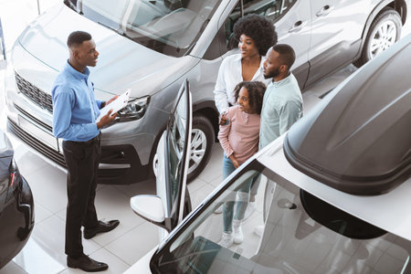 Car sales business concept. Above view of manager talking to Afro family with cute kid, selling auto...