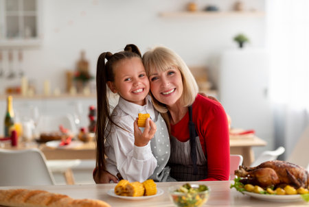 Happy senior woman embracing her granddaughter while cooking festive family dinner at home