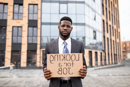 Young black businessman holding cardboard sign with the text LOOKING FOR A JOB, lost his job due to quarantineの写真素材