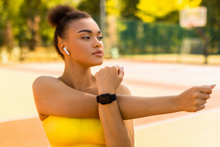 Sporty black woman in yellow sportswear stretching arms