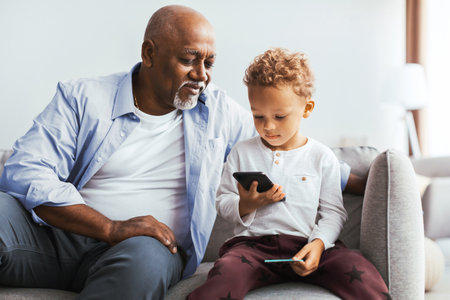 Grandfather and Grandson Share a Moment While Looking at a Smartphone in Their Home Living Room