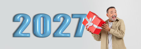 Excited Man Holds a Gift in Front of Large Year 2027 Signの写真素材