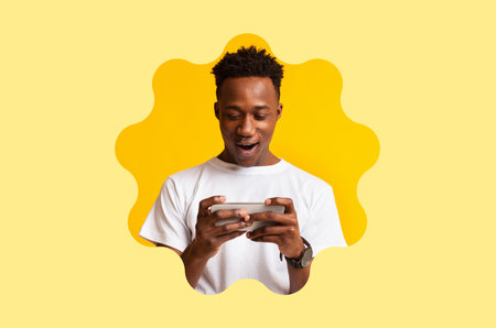 Young Man Enjoys Playing a Mobile Game While Smiling Against a Bright Yellow Background