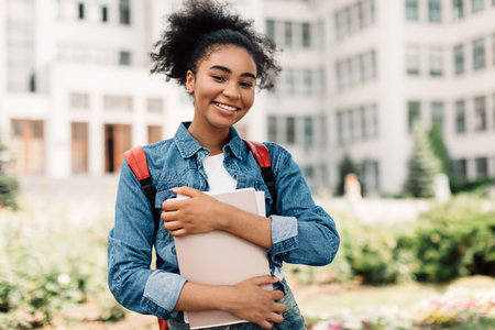 Happy African American Teenager Girl Posing Near Modern University Buildingの写真素材