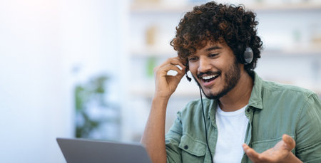 Young Man Using a Headset While Talking on a Laptop at a Work Desk During the Day