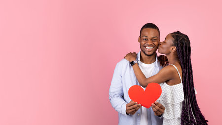 Young Romantic Black Couple Kissing And Holding Red Paper Heartの写真素材