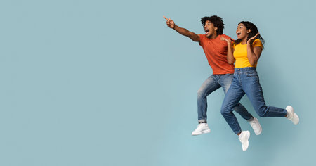 Carefree black millennial man and woman jumping in the airの写真素材