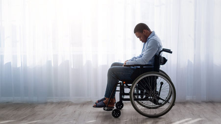 Man Using a Wheelchair Sitting Alone in a Bright Room With Natural Light Streaming Inの写真素材