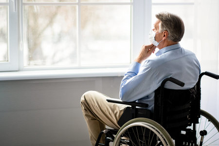Senior Man in a Wheelchair Looks out the Window While Thinking in Bright Indoor Spaceの写真素材