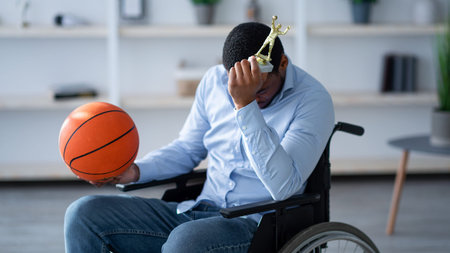 Man Using a Wheelchair Holds a Basketball and Trophy in a Modern Roomの写真素材