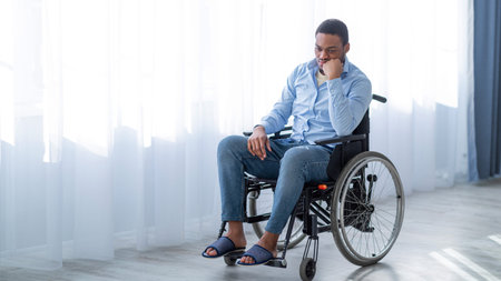 Young Black Man Sitting in a Wheelchair, Smiling and Thinking in a Bright Roomの写真素材