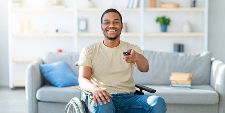Man Using a Wheelchair Enjoys Leisure Time at Home and Watches Televisionの写真素材