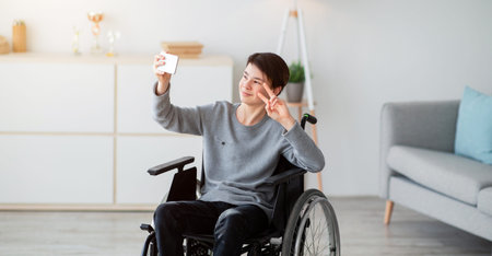 Young Man Using a Wheelchair Takes a Selfie in a Bright Living Room Settingの写真素材