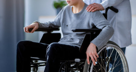 Supportive Healthcare Professional Assists Young Boy Using a Wheelchair in a Clinical Settingの写真素材