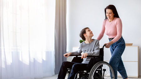 Woman Assists Boy Using a Wheelchair in a Bright Room With Large Windows and Soft Curtainsの写真素材