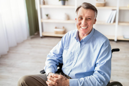 Senior Man With Gray Hair Smiles While Sitting in a Wheelchair in a Bright Roomの写真素材