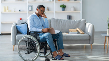 Man Using a Wheelchair Reads Notes While Sitting in a Modern Living Room Settingの写真素材