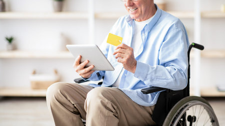 Senior Man Using Tablet While Sitting in Wheelchair and Holding a Credit Card Indoorsの写真素材