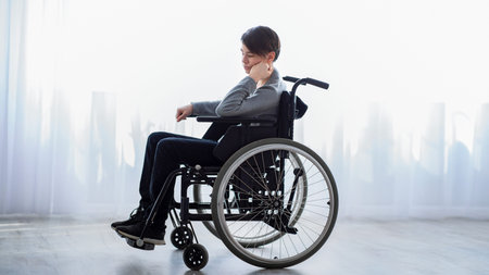 Young Boy Using a Wheelchair in a Bright Room Looking Thoughtful and Relaxedの写真素材