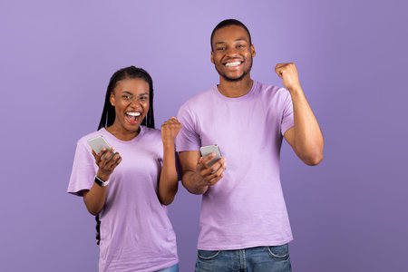 Black couple using phone celebrating success shaking fists