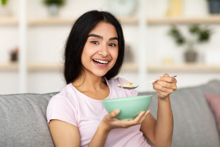 Healthy diet, weight loss concept. Smiling Indian lady eating cereal, having nutritious breakfast at...