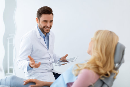 Cheerful man dentist having conversation with blonde woman patientの写真素材