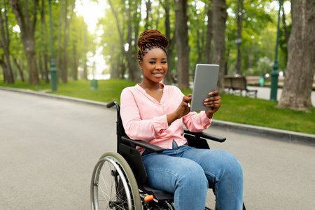 Happy impaired young woman in wheelchair using tablet computer for online communication outdoorsの写真素材
