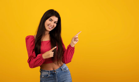 Happy young armenian lady pointing two fingers aside at free space advertising your text or design, yellow backgroundの写真素材