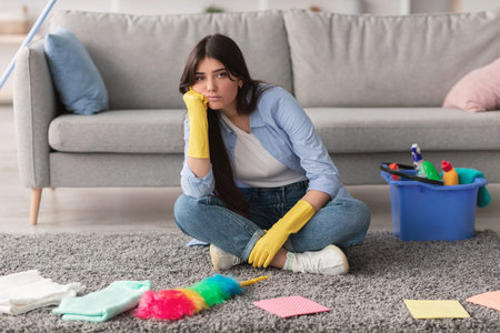 Upset woman tired of cleaning sitting on floorの写真素材