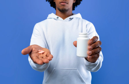 Unrecognizable black teen holding jar with meds and pills in hands on blue background. Coronavirus, cold, flu treatmentの写真素材