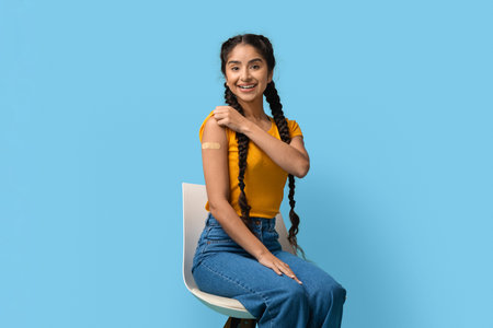 Young Woman Happily Showing off Bandage After Getting Vaccination in Bright Blue Roomの写真素材