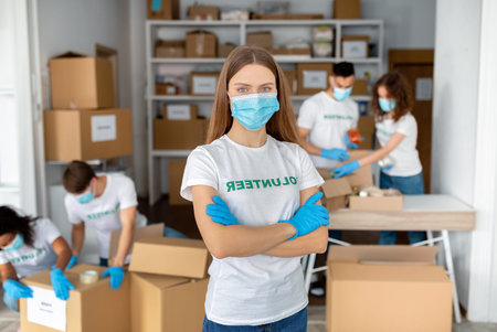 Young Woman Volunteers at Charity Center While Colleagues Pack Donation Boxesの写真素材