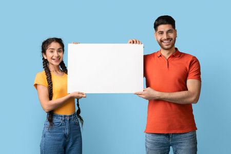 Two Friends Smiling and Holding a Blank Sign Against a Blue Background, Ready for a Fun Announcement...