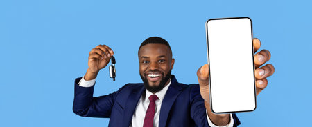 Happy Businessman Showing Smartphone and Car Keys Against Blue Backgroundの写真素材