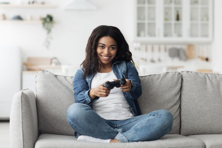 Fun stay home pastimes. Joyful african american woman using joystick to play online video games,...