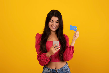 Mobile banking concept. Excited armenian woman holding smartphone and credit card, using application...